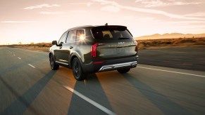 A dark-green 2022 Kia Telluride travels on a two-lane highway through a desert at sunset