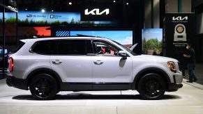 A white 2022 Kia Telluride in a building with the Kia logo in the background above the car.