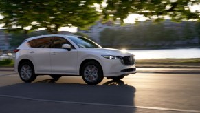 A white 2022 Mazda CX-5 2.5 Turbo Signature traveling on a road past a a waterway and buildings