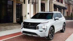 A white 2022 Mitsubishi Outlander compact crossover SUV parked on a brick road outside a brick storefront