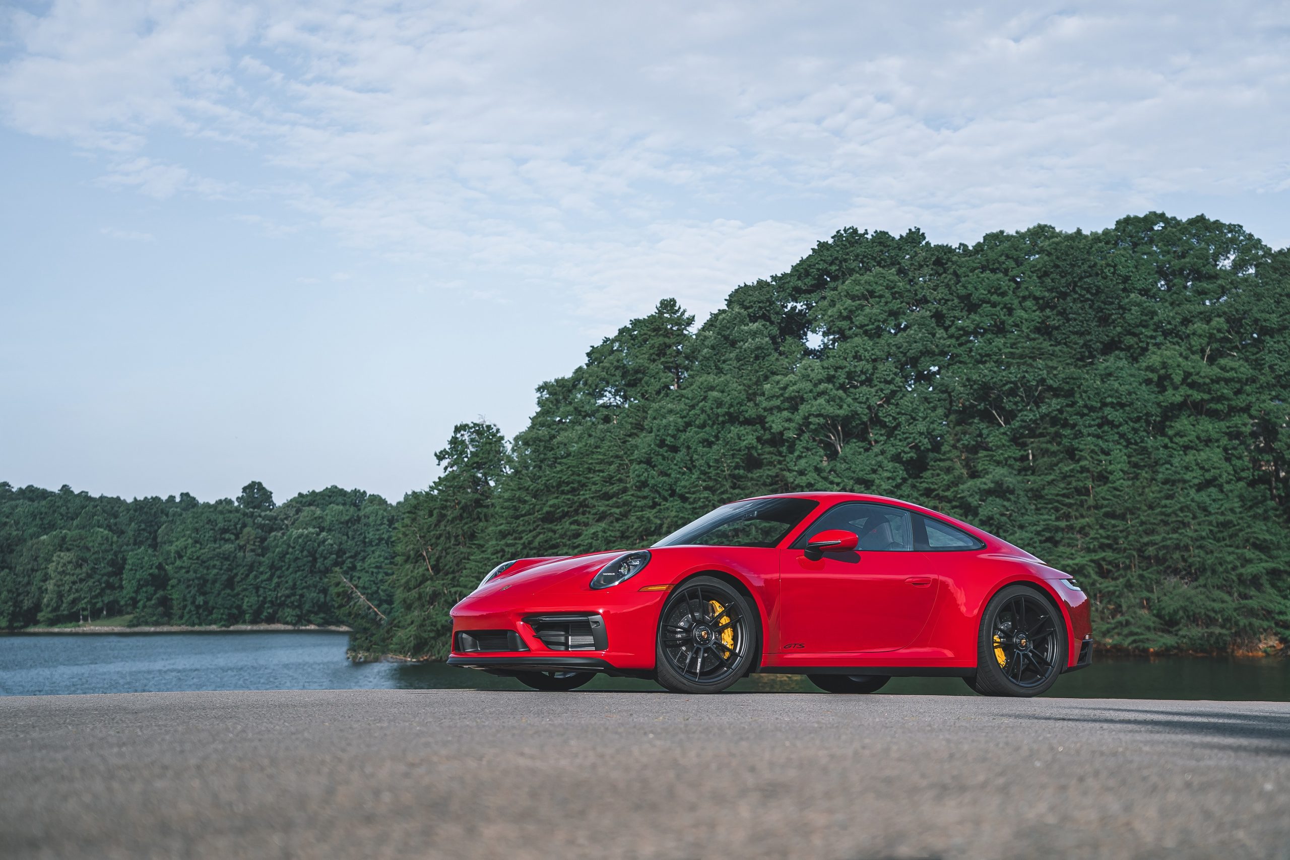 A red Porsche 911 GTS shot from the front 3/4 on a lake shore