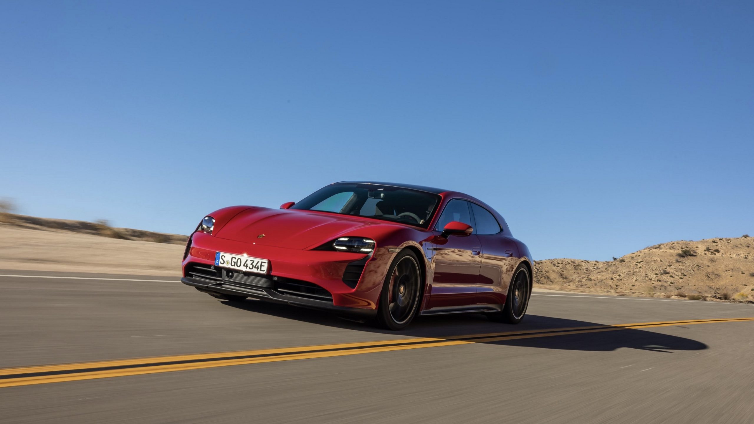 A red 2022 Porsche Taycan GTS Sport Turismo drives on a desert road