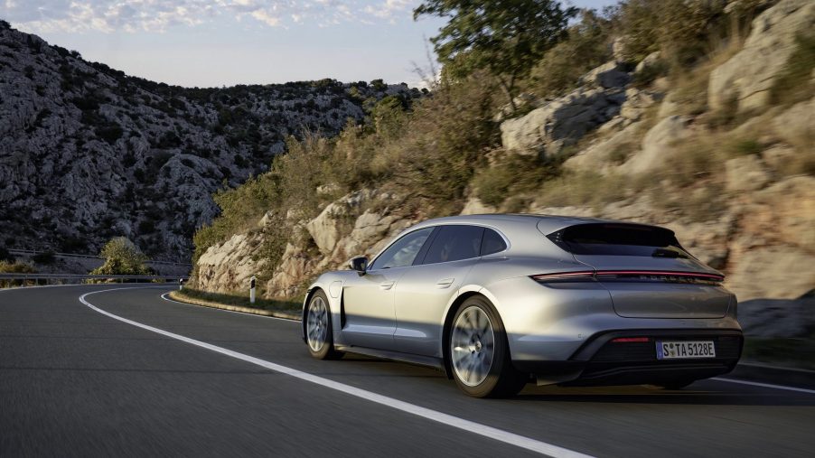 The rear 3/4 view of a silver 2022 Porsche Taycan Sport Turismo driving on a mountain road