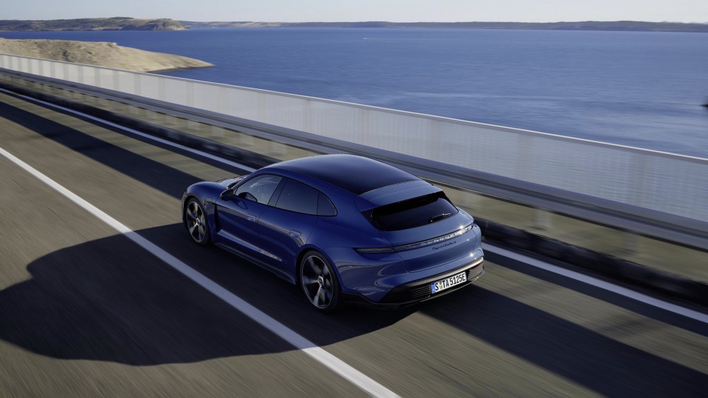 The overhead rear 3/4 view of a blue 2022 Porsche Taycan Turbo S Sport Turismo driving by the ocean