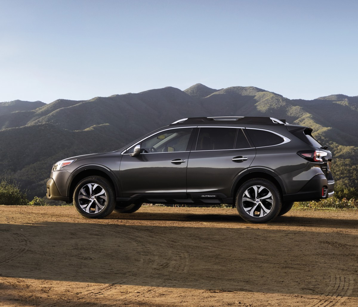 A profile view of a grey Subaru Outback in front of mountains.