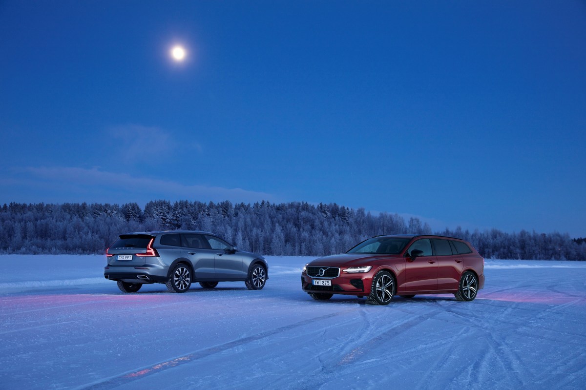 A grey Volvo V60 Cross Country sits next to a red Volvo V60 T8 on a snow and ice-covered lake. 