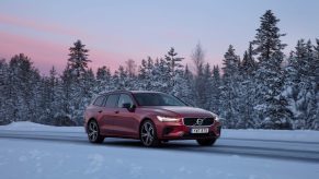 A 3/4 front view of a red Volvo V60 Recharge on a snow covered road with trees in the background.