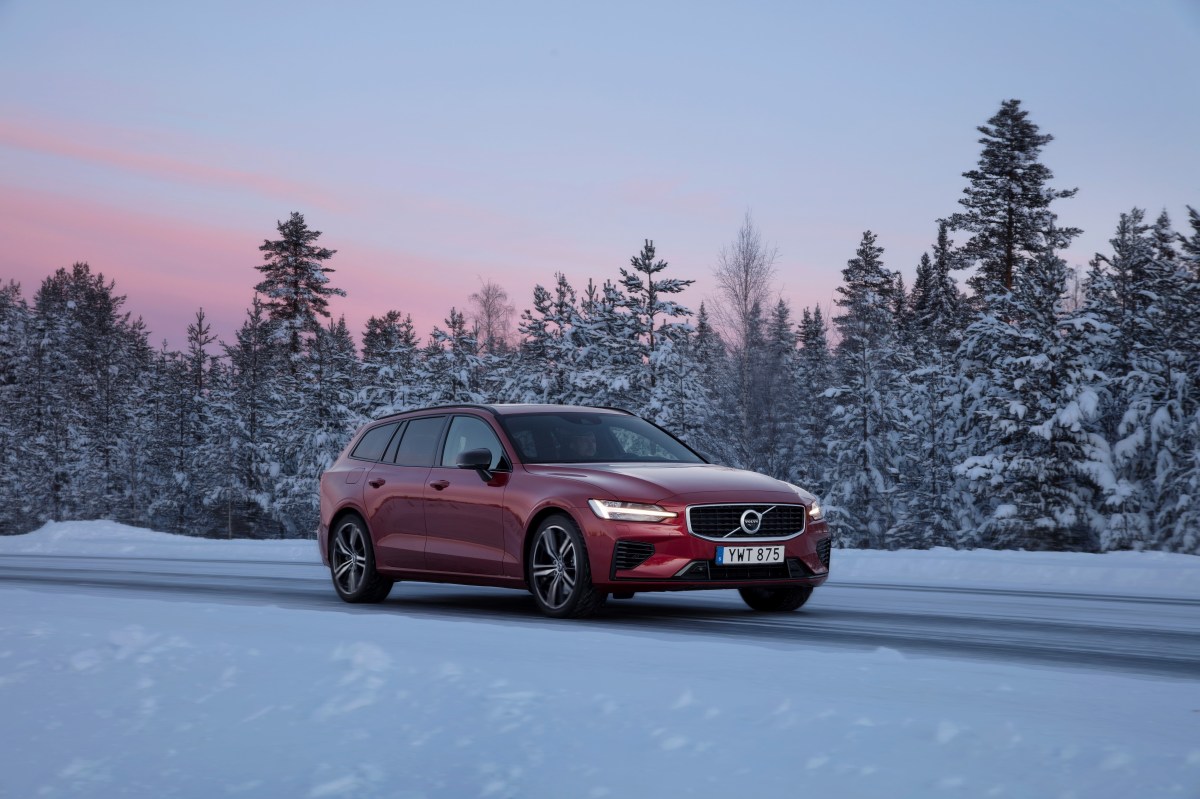 A 3/4 front view of a red Volvo V60 Recharge on a snowy road with snow-covered trees in the background.