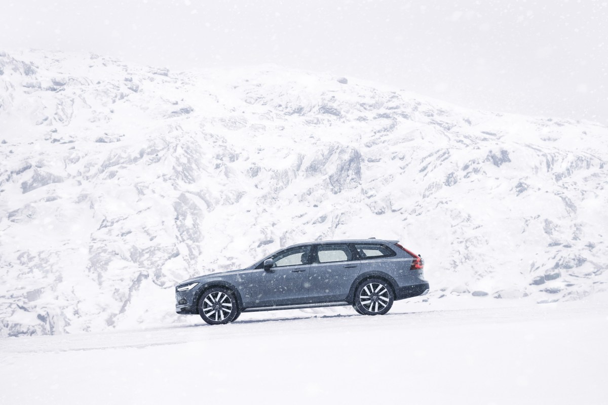 A profile view of a blue-ish grey Volvo  V90 Cross Country in front of snow-covered mountains. 