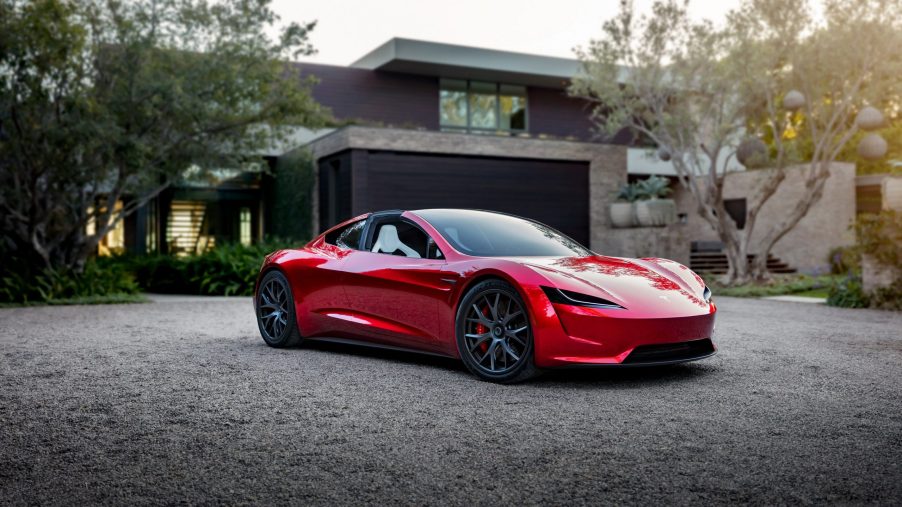 A red Tesla Roadster EV shot from the front 3/4 in front of a house