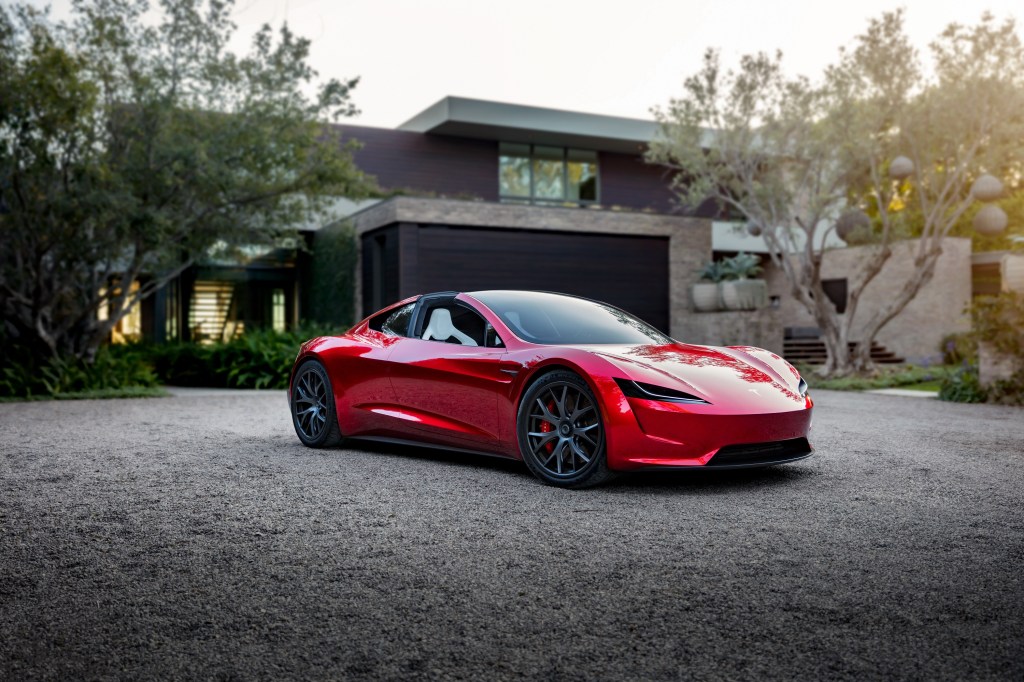 A red Tesla Roadster EV shot from the front 3/4 in front of a house