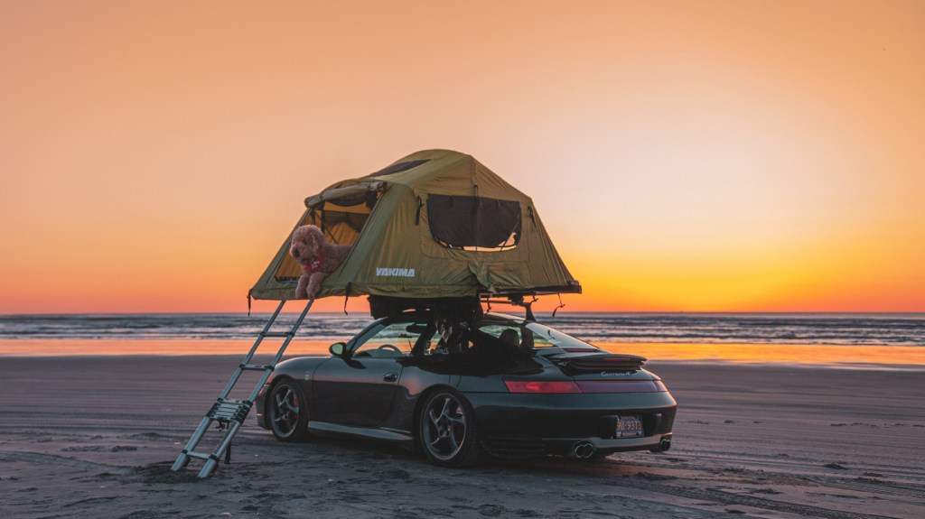 The rear 3/4 view of a gray 996 Porsche 911 Carrera 4 with a roof tent on a beach