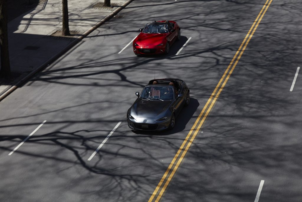 A gray 2022 Mazda MX-5 Miata RF and a red 2022 Mazda MX-5 Miata convertible drive down a city street