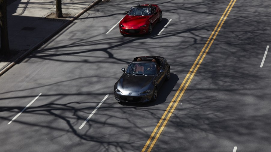 A gray 2022 Mazda MX-5 Miata RF and a red 2022 Mazda MX-5 Miata convertible drive down a city street
