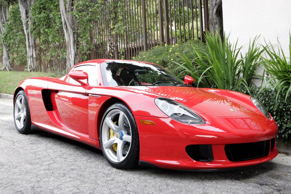 A Guards Red Porsche Carrera GT parked on a tree-lined drive