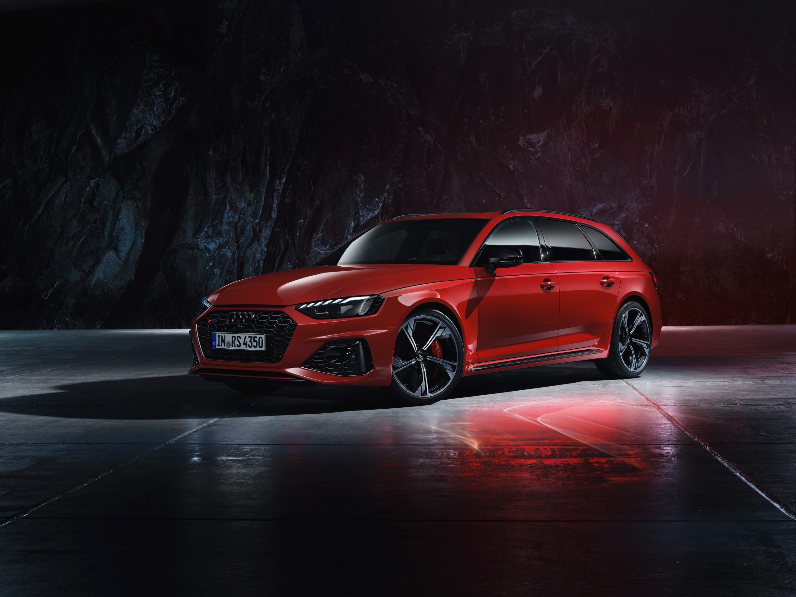 A 3/4 front view of a red 2022 Audi RS4 Avant parked in front of a dark rock wall