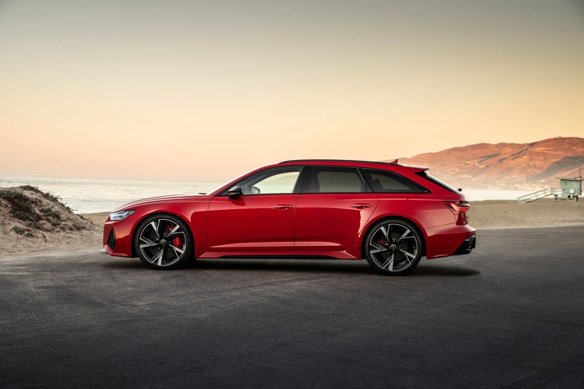 A profile view of a red Audi RS6 Avant in front of a beach.