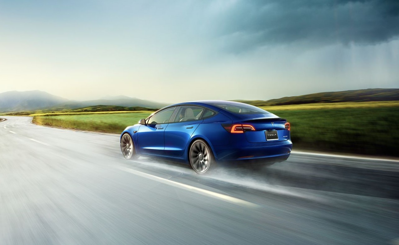 Blue 2022 Tesla Model 3 driving on a wet road, highlighting 2022 EVs that make an impact on climate change