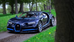 A blue-on-blue Bugatti Chiron, one of the fastest cars in the world, shot from the 3/4 angle among trees