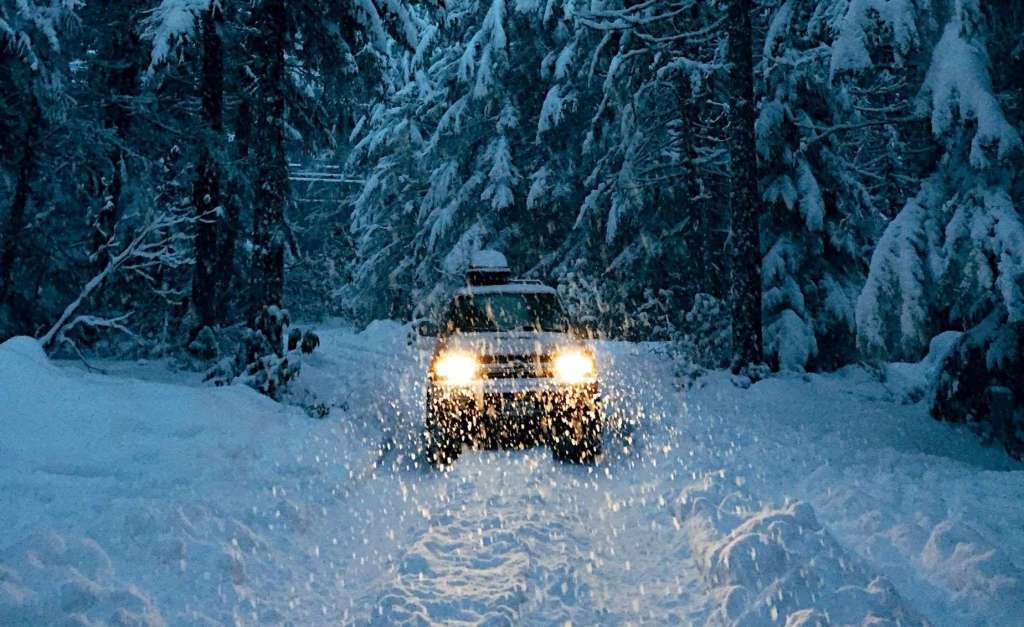 Car warms up with headlights on a snowy path in the forest 