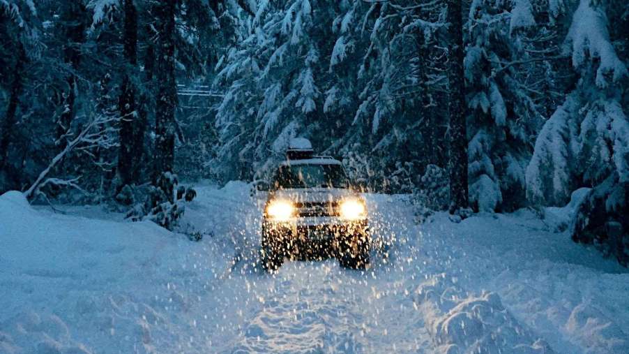Car warms up with headlights on a snowy path in the forest