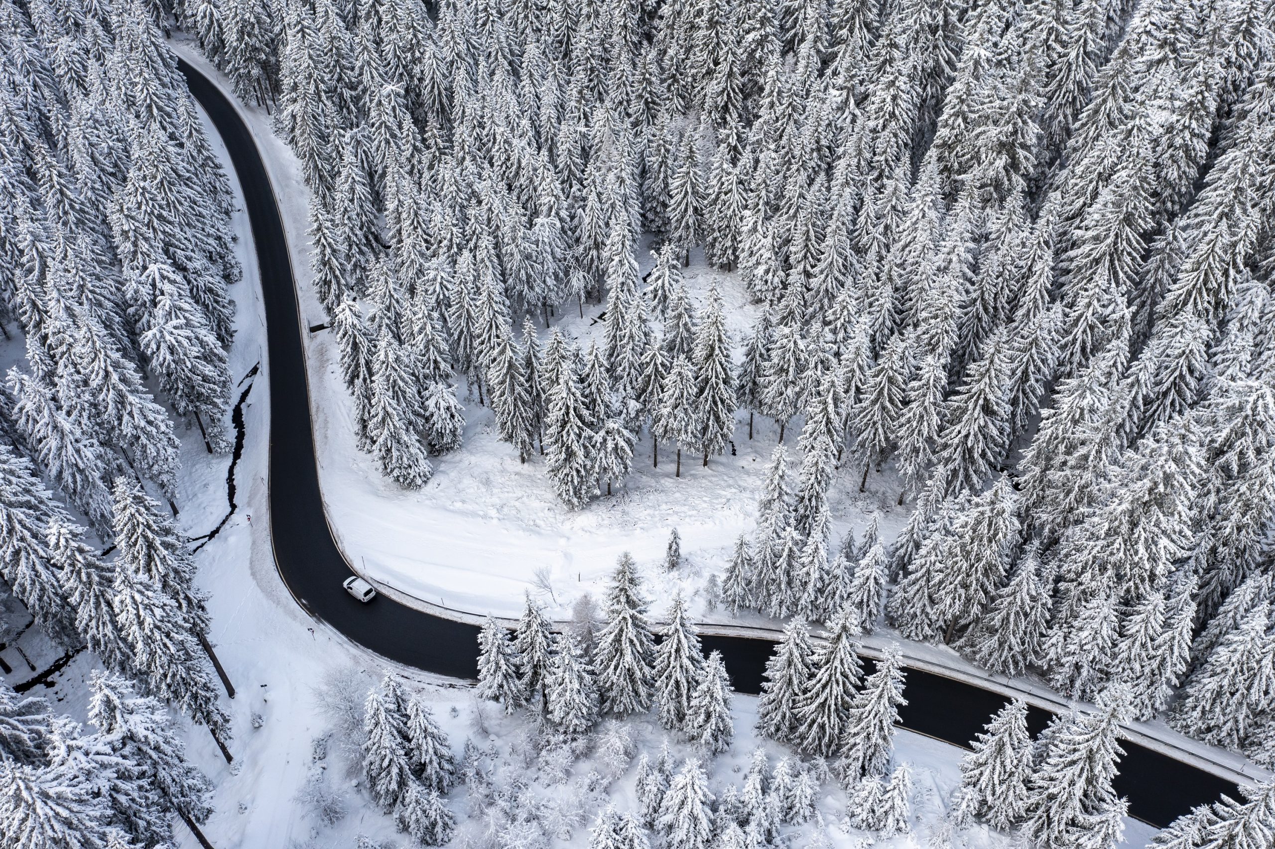 A car travels down an empty winding road in winter