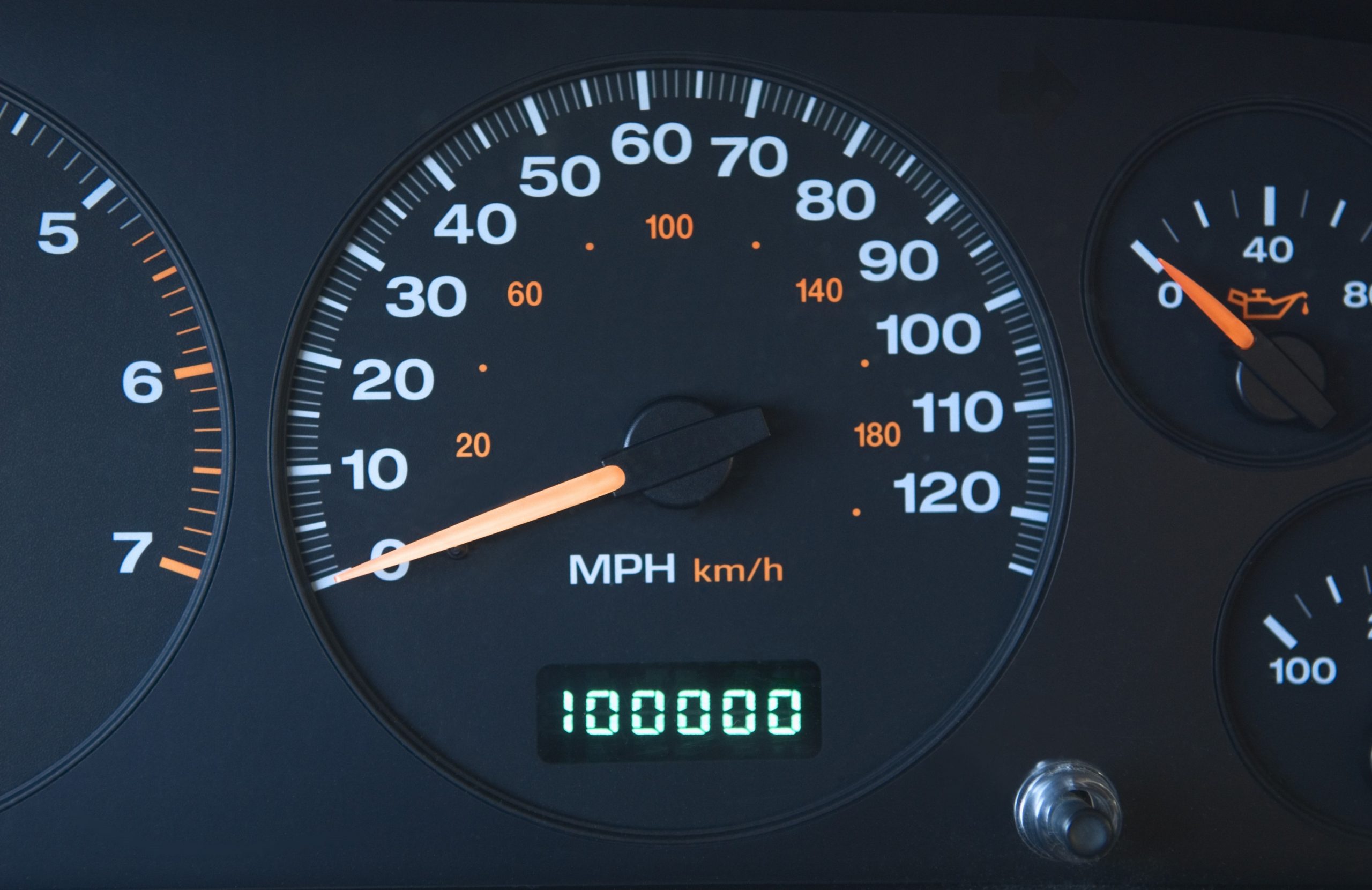 A car's gauge cluster, free of check engine lights, reads 100,000 miles