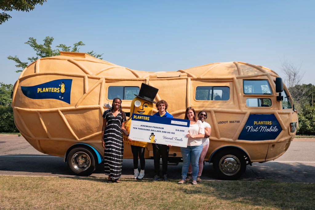 Mr. Peanut hands a donation check to an organization in front of the Nutmobile.