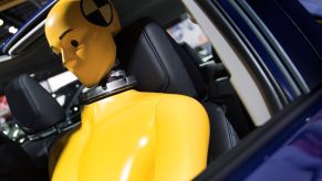 A yellow crash test dummy sitting in a car prepared for a crash test.