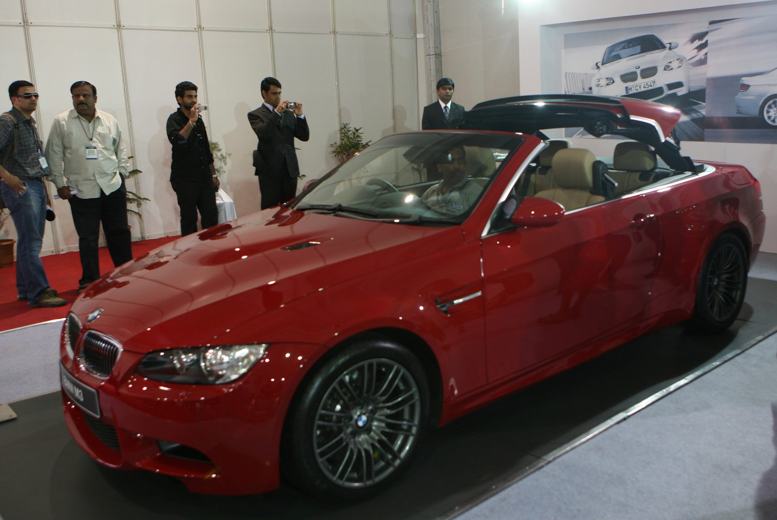 A red E92 M3 retracts its convertible top at a motor show