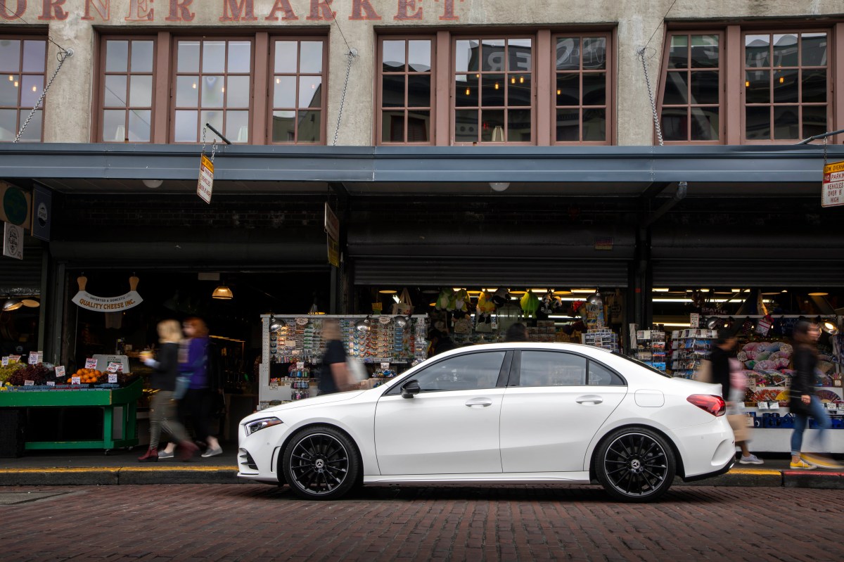 A profile view of a white Mercedes-Benz A220 sedan in front of a market