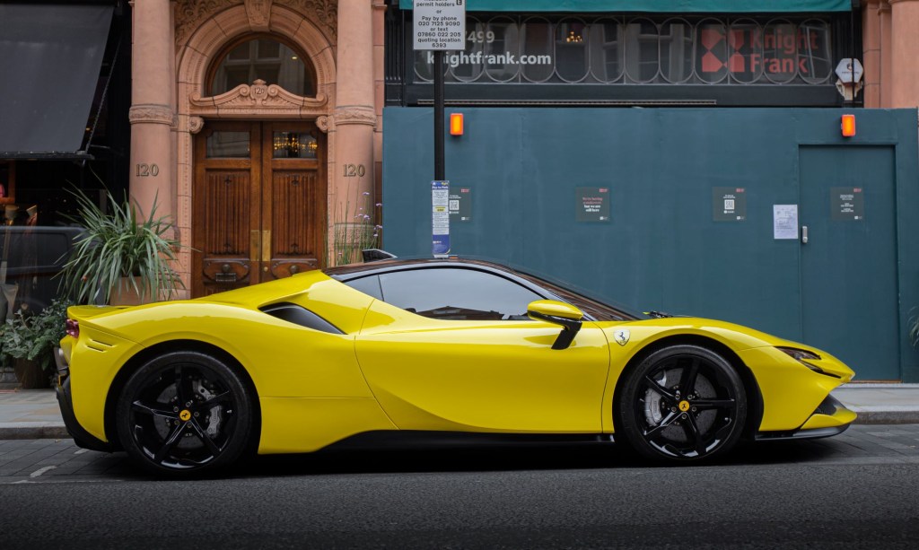 A yellow Ferrari SF90 parked in front of a stone building with large green doors. 