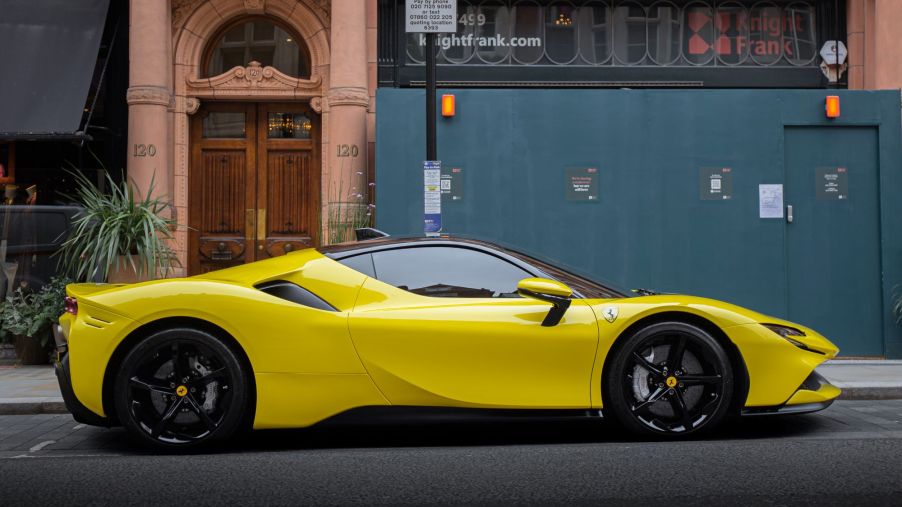 A yellow Ferrari SF90 parked in front of a stone building with large green doors.