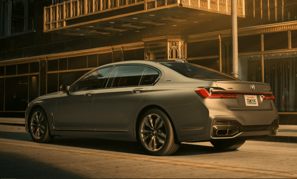 Fully loaded new gray 2022 BMW 7 Series M760i xDrive Sedan driving by a large building