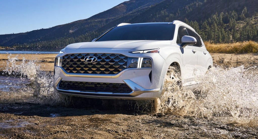 A white 2022 Hyundai Santa Fe is driving through mud and water. 