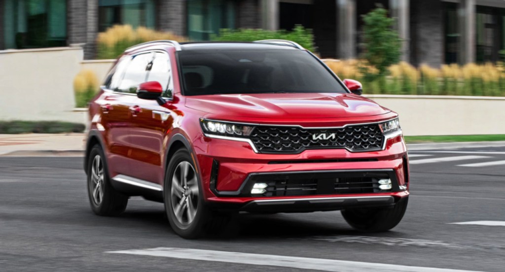 A red 2022 Kia Sorento Hybrid SUV is driving in a parking lot. 