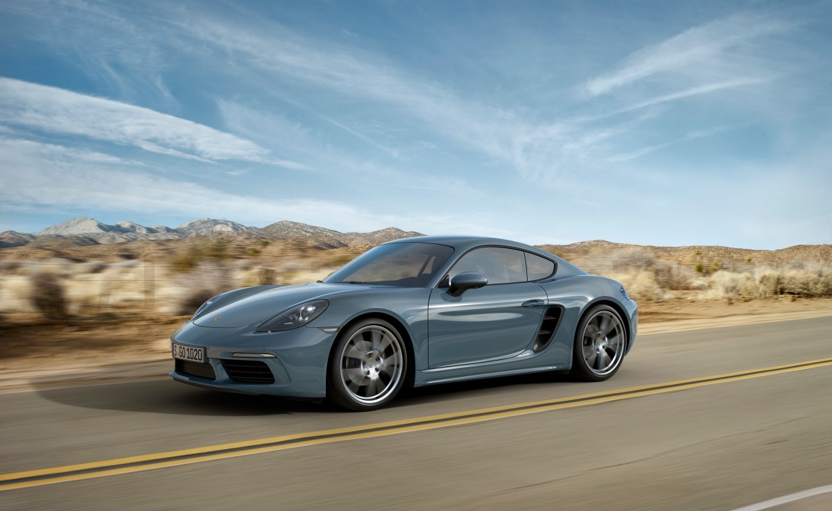 A 3/4 front view of a blue/gray Porsche 718 Cayman driving on a desert road