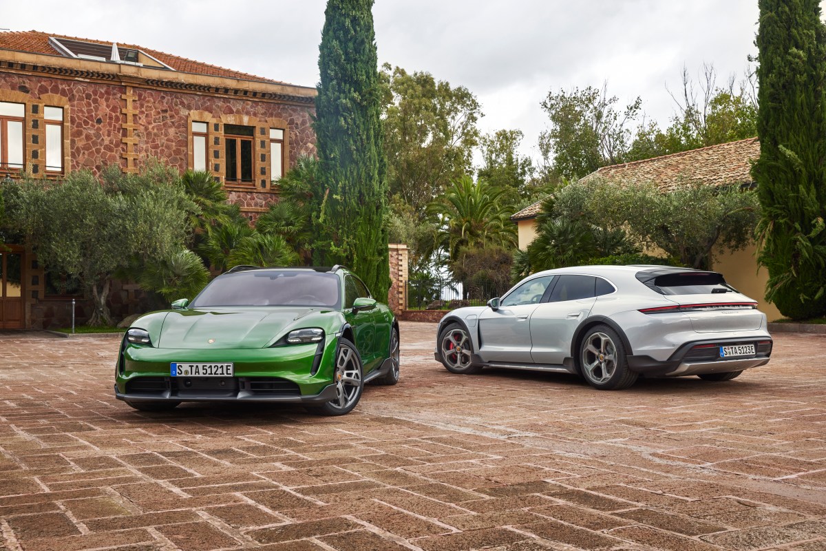 A green and silver Porsche Taycan Cross Turismo sit next to each other in front of a house.