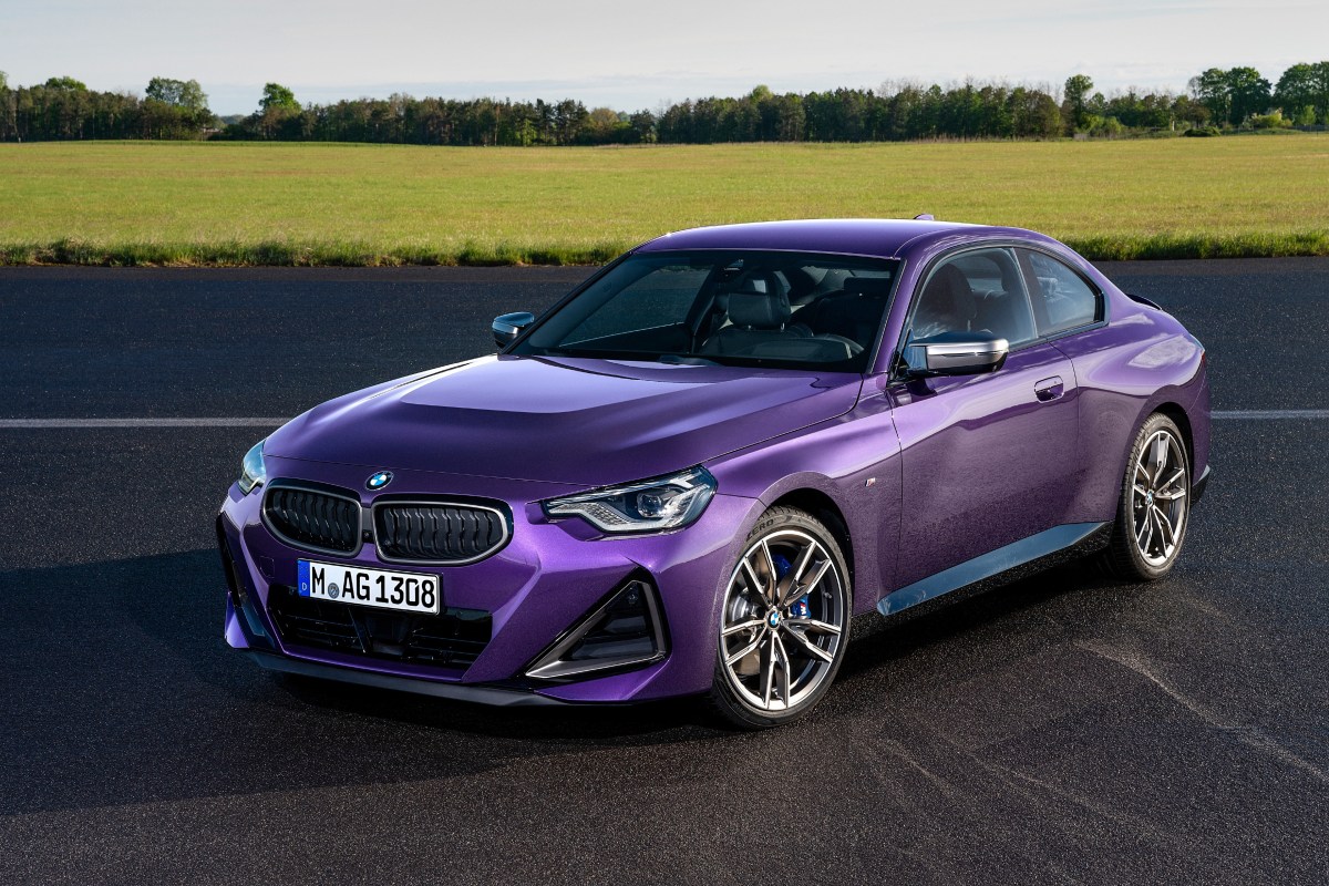 A Thundernight Purple 2022 BMW 2 Series Coupe sits on a road with a field and trees in the background