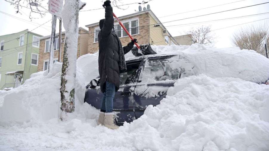 Person shoveling snow off a car, highlighting story about an electric vehicle warming up a cabin in cold weather