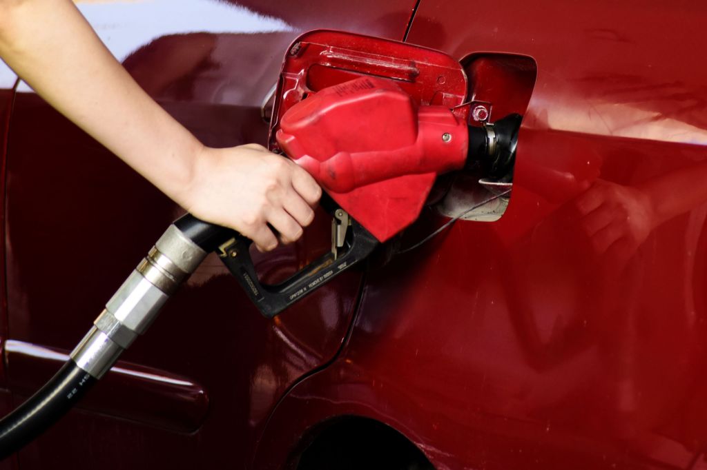 A person pumping fuel, such as gasoline, diesel, jet fuel, or more, into a red vehicle.