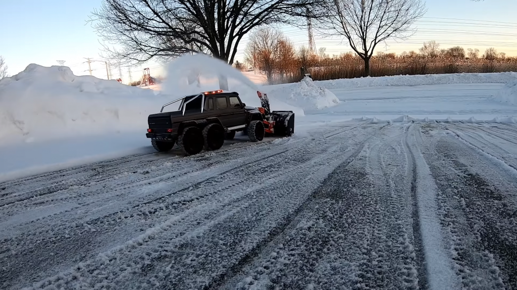 An RC Mercedes with a snow blower attachment clears a driveway of a winter dusting