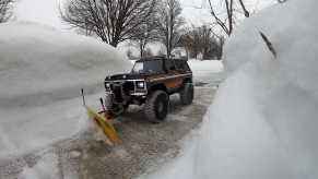 An RC Ford Bronco with a snow plow attachment clears a driveway of snow in the winter