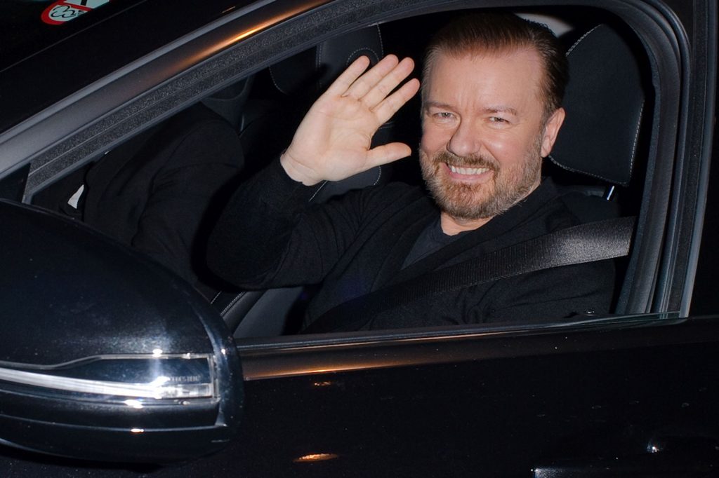 Ricky Gervais waving from a black car. 