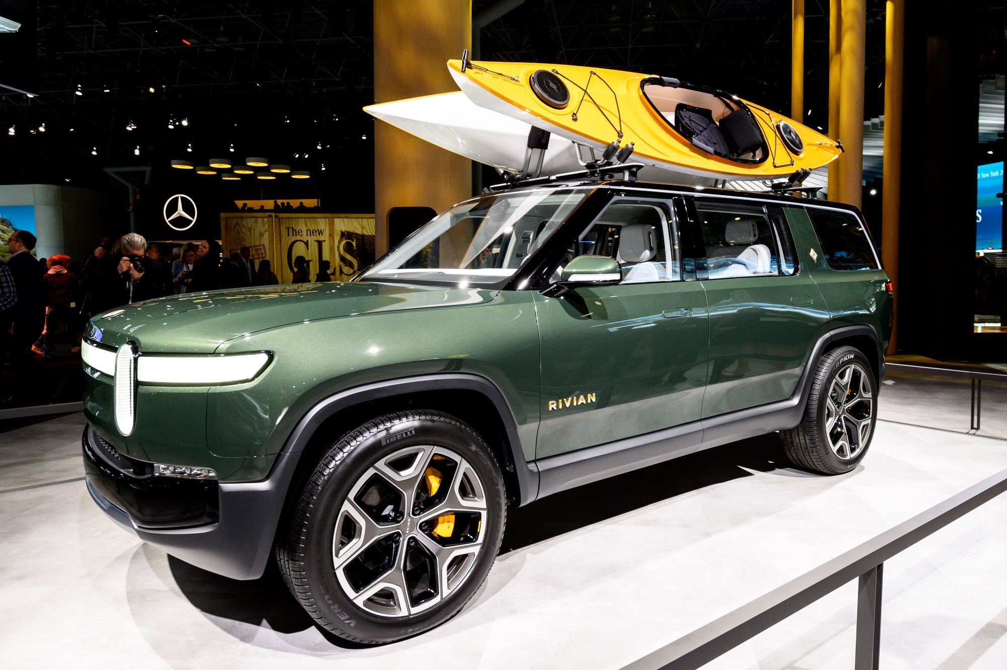 A green Rivian R1S with two canoes on top of the car.