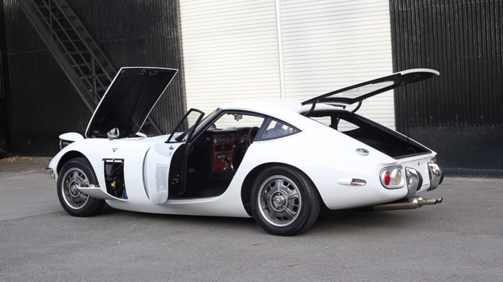 The rear 3/4 view of a white Rocky Auto Toyota 2000GT replica with its doors and panels open