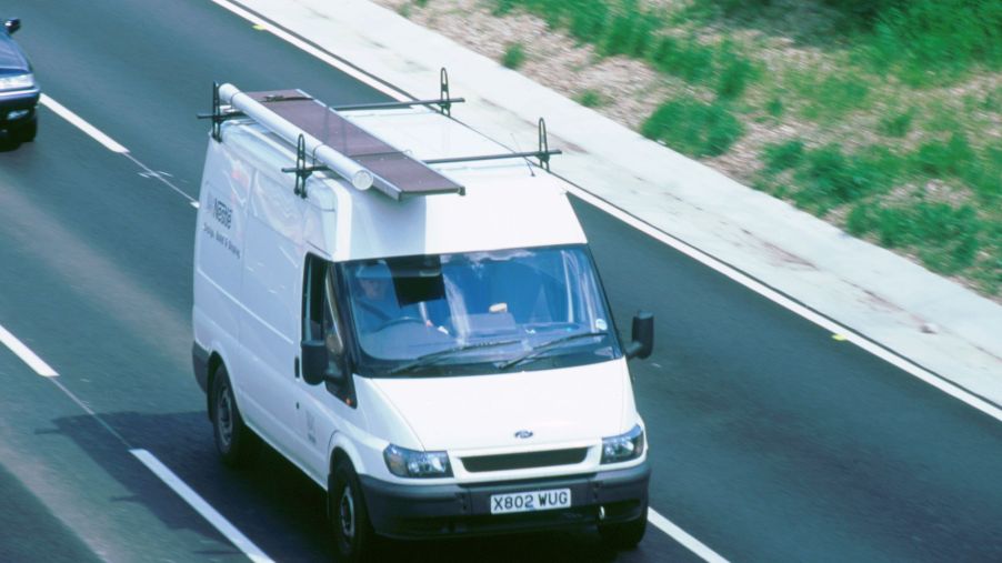 A white van with a roof rack on top driving down the highway.