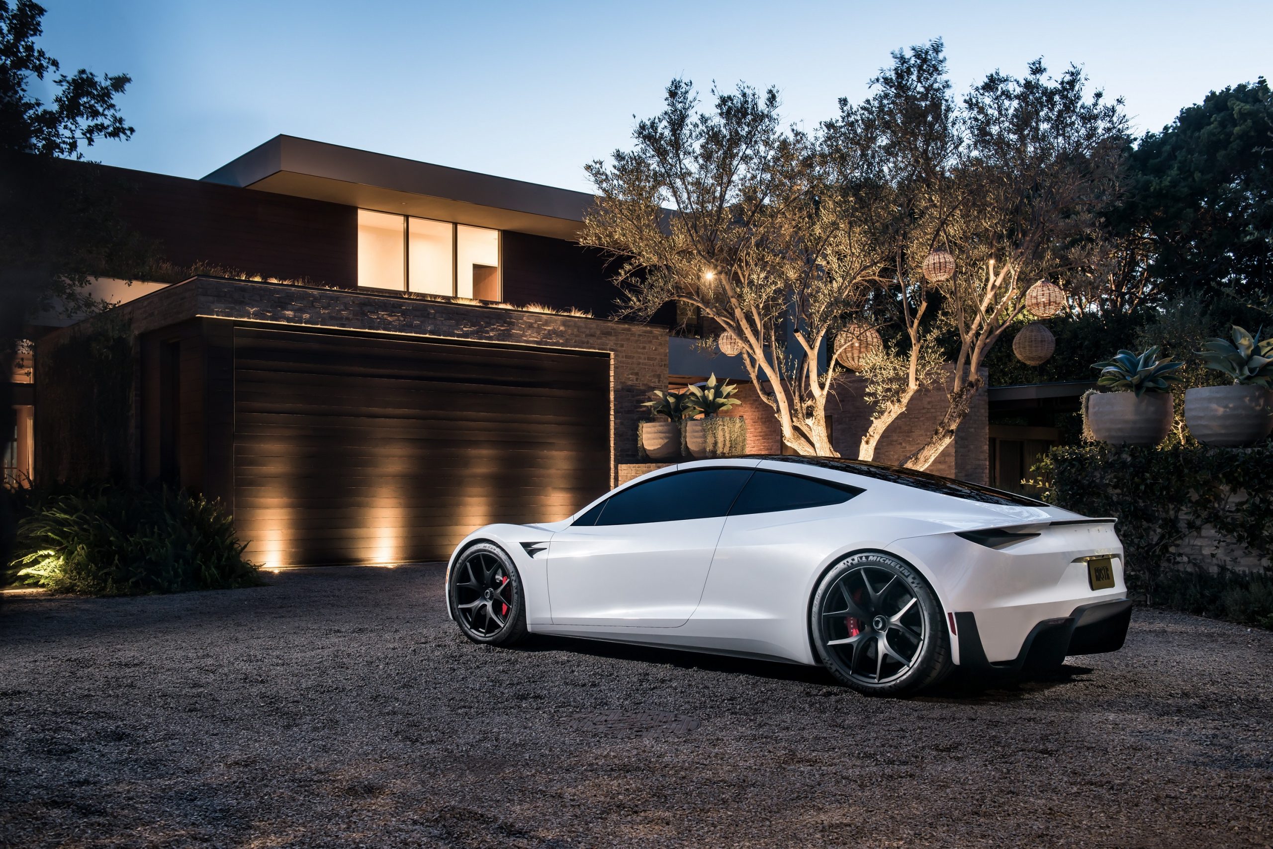A white Tesla Roadster shot from the rear 3/4 angle in front of a house