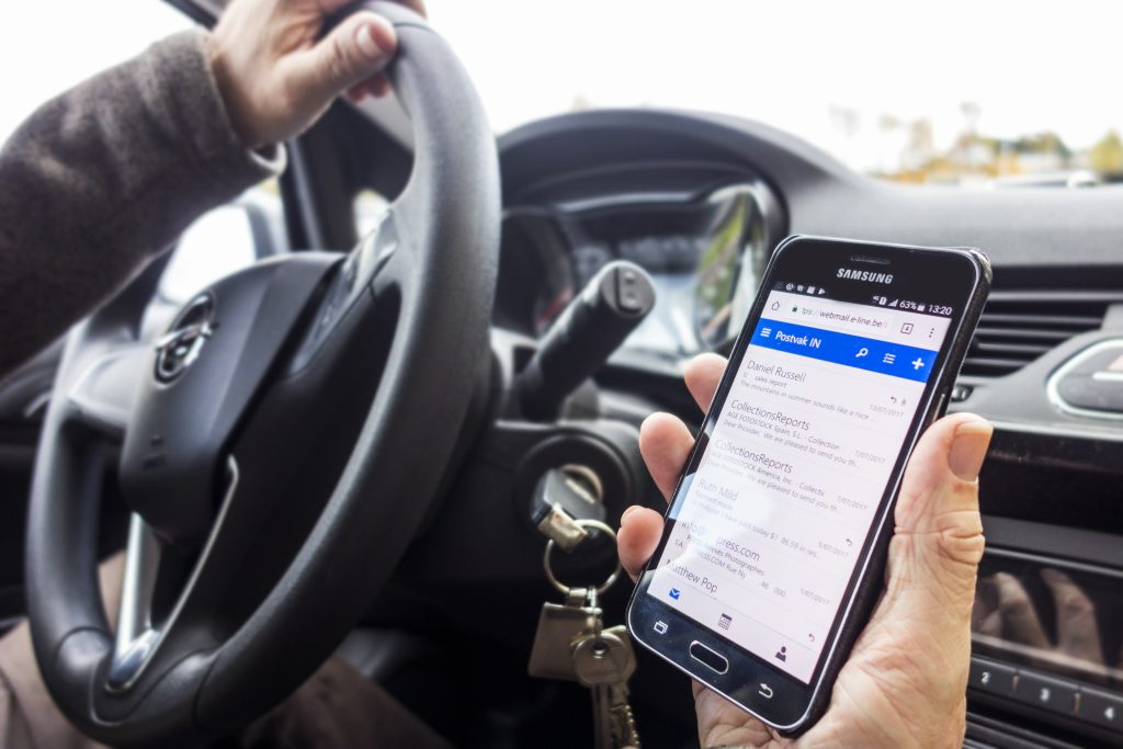 A person texting and driving, which can result in accidents which will raise the costs of car insurance for you and your family.