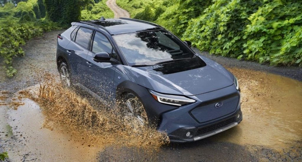 A blue 2023 Subaru Solterra is driving through mud. 